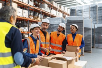 Group of happy diverse workers wearing safety vests and hard hats collaborating on packaging