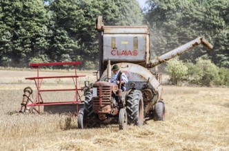 Older tractor-drawn Claas combine harvester harvesting wheat at old-fashioned harvest festival in