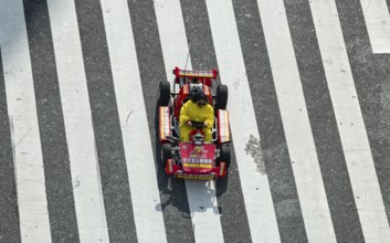 People in costumes drive small go-kart racing cars across zebra crossings, Shibuya Crossing,