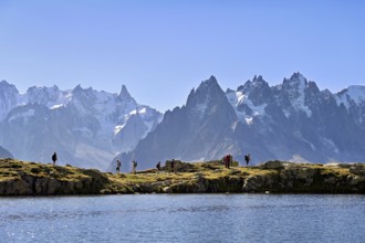 A group of hikers at Lac de Chésserys, behind the snow-covered Mont Blanc massif,