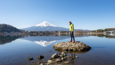 Young man standing on a rock in water, volcano Mt. Fuji is reflected in Lake Kawaguchi, Yamanashi