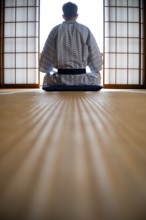 Young man wearing kimono sitting in traditional Japanese living room with tatami mats and shoji