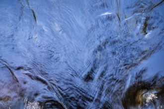 Shimmering blue water surface of a stream, current, light reflections, abstraction, long exposure,