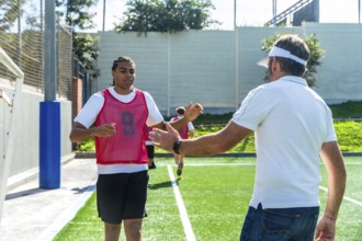 Soccer coach extends a hand to a young male player wearing a number 9 bib on a green artificial