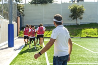 Soccer coach watches youth team warming up on artificial turf, guiding drills and preparation for