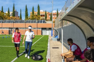 Soccer coach and young player walking on a green artificial turf field after training, carrying