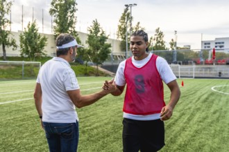 Soccer coach and young player shaking hands on an artificial turf field, demonstrating teamwork,
