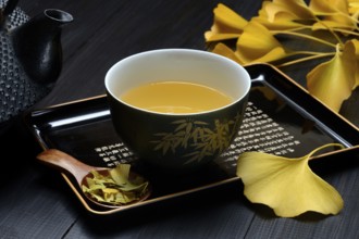 Ginkgo tea in tea bowl and ginkgo leaf, tea leaves in a spoon, ginkgo biloba