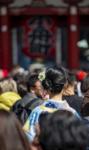 Young Japanese woman wearing kimono surrounded by numerous visitors on Nakamise-dori shopping
