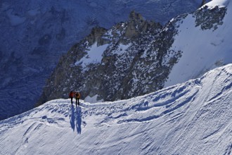 Two ascended mountaineers run across a snow-covered mountain ridge, Aiguille du Midi,