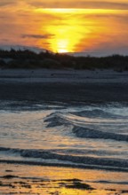 Sunset on a quiet beach with soft light on the waves, wet beach at low tide, dunes in the
