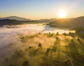 Sunrise over a fog covered village in a rural landscape, golden morning light, serene autumn