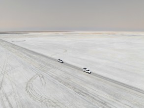 Aerial view, two off-road cars driving on a salt pan, arid landscape, Botswana