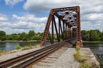 Railroad tracks leading to old rusted Terrebonne Pratt truss railroad bridge over Des Mille-Iles