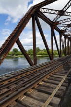 Railroad tracks leading to old rusted Terrebonne Pratt truss railroad bridge over Des Mille-Iles