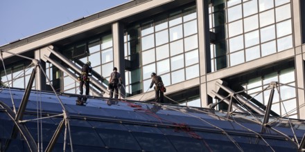 Three male glass cleaners abseiling down a glass roof of Berlin Central Station to clean windows,