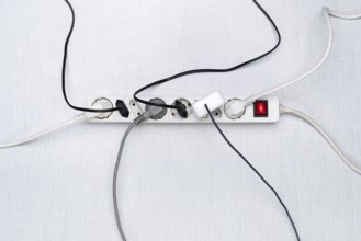 Top view of a power strip with on/off switch and various plugged-in plugs and cables on a white