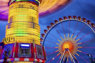 Illuminated chain carousel in motion, behind the Ferris wheel at standstill, Festwiese,