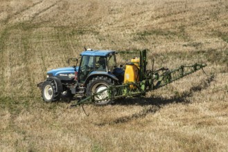 Tractor spreading fertilizer on harvested stubble field in Ystad municipality, Skåne county,