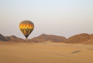 The hot-air balloon above an arid plain and isolated mountain ridges at the edge of the Namib