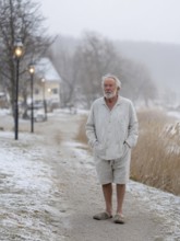 An elderly man in pyjamas stands in a cold, wintry environment, looking confused, helpless and
