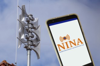 (Photomontage) Close-up of a siren, next to it the open warning app NINA on a smartphone