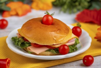 A filled bagel on a plate, decorated with tomatoes on a yellow cloth