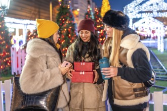 Three friends enjoying christmas time together, holding christmas gifts and a reusable cup at the