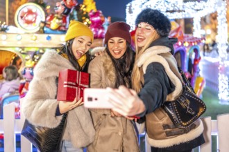 Three happy female friends taking a selfie with a smartphone at a christmas market amusement park,