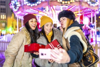 Three cheerful multi ethnic women taking a selfie with christmas presents at the christmas market
