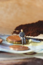 Miniature figure of a man sitting on coins and banknotes, ground coffee in a filter bag in the