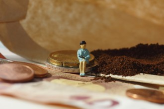 Miniature figure of a woman sitting on coins and banknotes, ground coffee in a filter bag in the