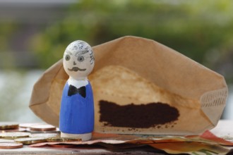 Male wooden cone figure with coins and banknote in front of filter bag with coffee North
