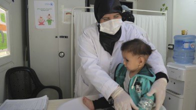 A doctor examining a refugee child for malnutrition in the camp using weight and height measurement