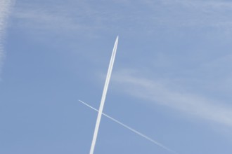 Two jet passenger aircraft with vapour trails or contrails flying in a blue sky crossing making a