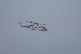 Sikorsky S-92A helicopter of the UK HM Coastguard flying in a blue sky, England, United Kingdom