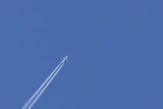 Jet passenger aircraft with a vapour trail or contrail flying in a blue sky, England, United