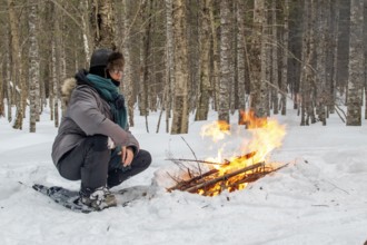 A woman warms herself by a campfire in winter, Gaspesie national park, Province of Quebec, Canada,