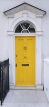 Bright yellow front door with neoclassical triangular pediment, Palladian-style entrance, white