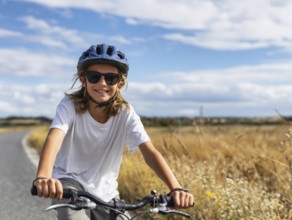 A girl with a bicycle helmet rides a bicycle and smiles friendly into the camera, AI generated, AI