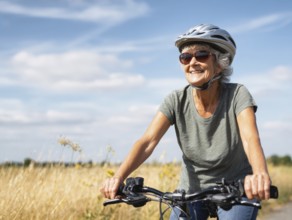 An elderly lady, a senior citizen with a bicycle helmet, rides a bicycle and smiles in a friendly