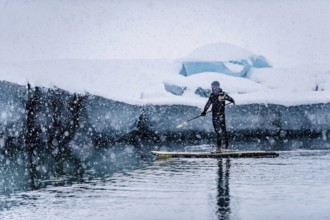 Man stand up paddling, snowfall, glacier lagoon Jökulsarlon at Vatnajökull, Iceland* Man stand up