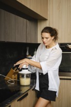 A woman skillfully blends banana and sea buckthorn fruits in a sleek kitchen. She carefully