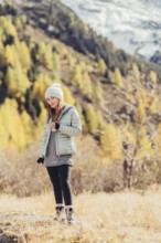 Woman in winter clothes in autumn Engadine with golden trees in Switzerland