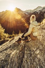 Woman sitting thoughtfully at a feslen at autumn atmosphere during sunset in the Swiss Alps in the