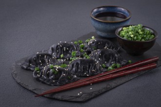Japanese gyoza dumplings, made of black dough, black gyoza, with green onions and sauce, on a