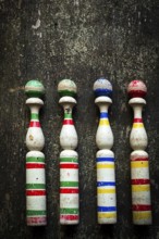 Four vintage wooden bowling pins with vibrant colors sit in a row on a rustic wooden surface,