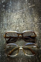 A collection of vintage eyeglasses rests on a rustic wooden surface, illuminated by warm lighting