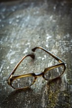 A pair of vintage glasses lies on a weathered wooden table. The unique design is illuminated by