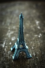 A striking teal miniature Eiffel Tower stands on a rustic wooden surface, bathed in soft lighting